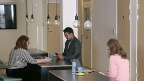 A modern office space with a long table, two chairs, and a laptop. There are light fixtures above the table and a door with the number 116. - Citysleep - Hostel (Luleå)