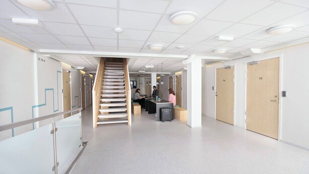 A modern interior with a central staircase, a reception desk, and a hallway leading to doors numbered 102-108 and 113. - Citysleep - Hostel (Luleå)