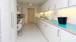 A narrow kitchen with white cabinets, a teal countertop, and a black bucket. - Citysleep - Hostel (Luleå)