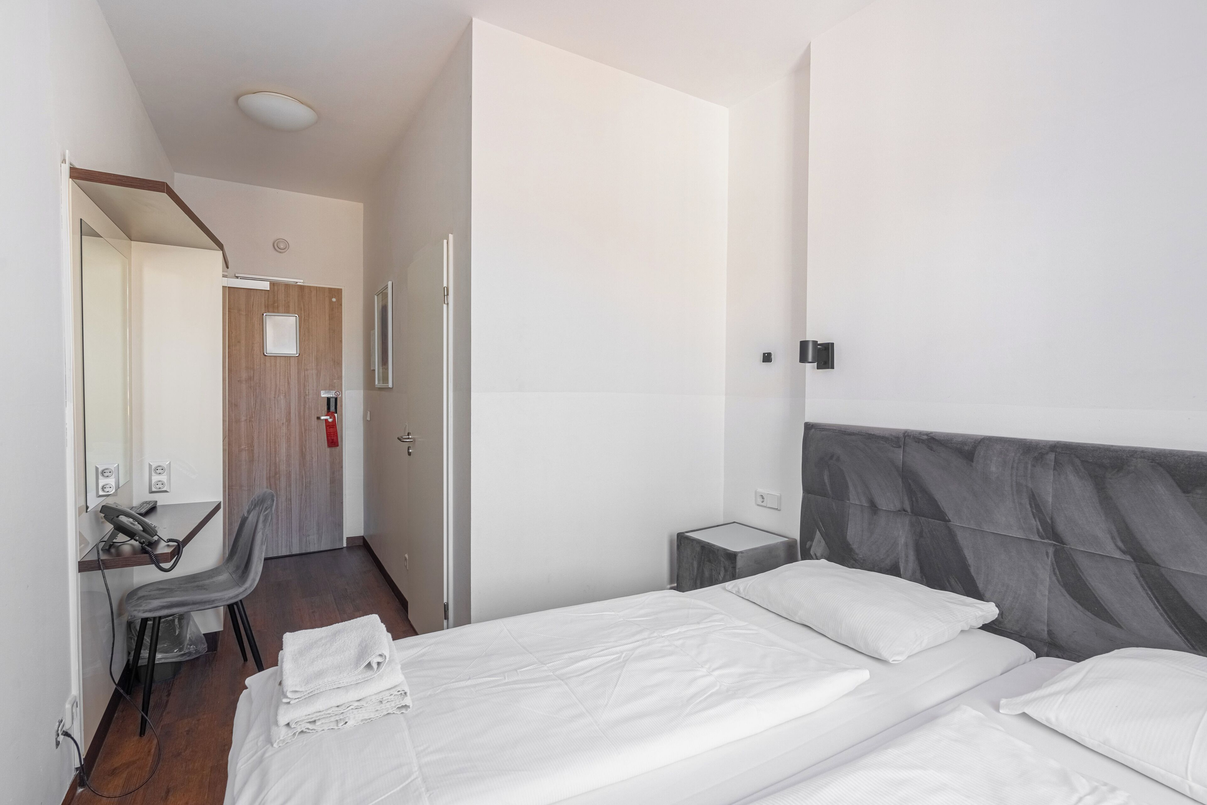 Una camera d'hotel con un letto, una scrivania, una sedia e un piccolo comodino.