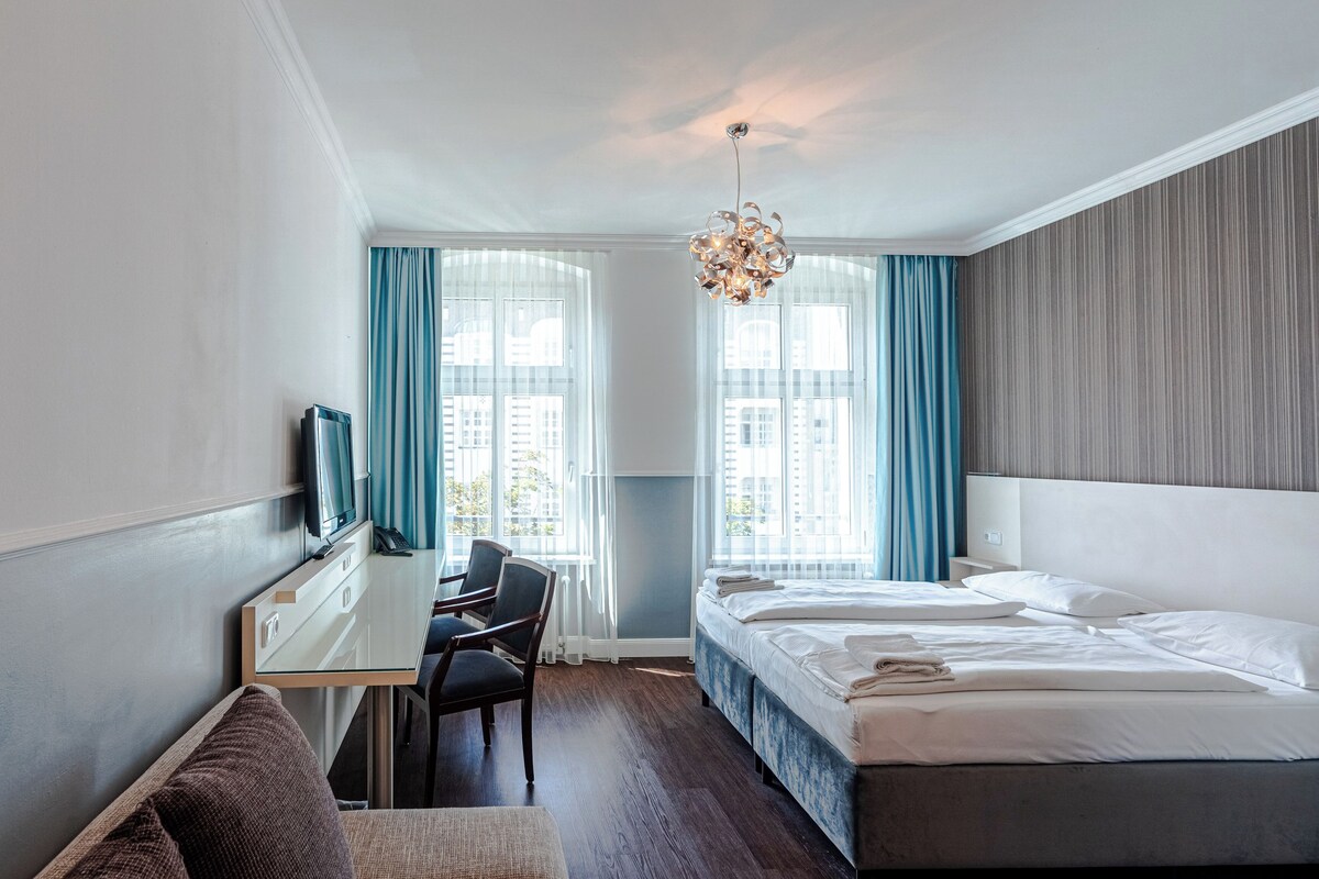A hotel room with a bed, a desk, a chair, and a TV.
