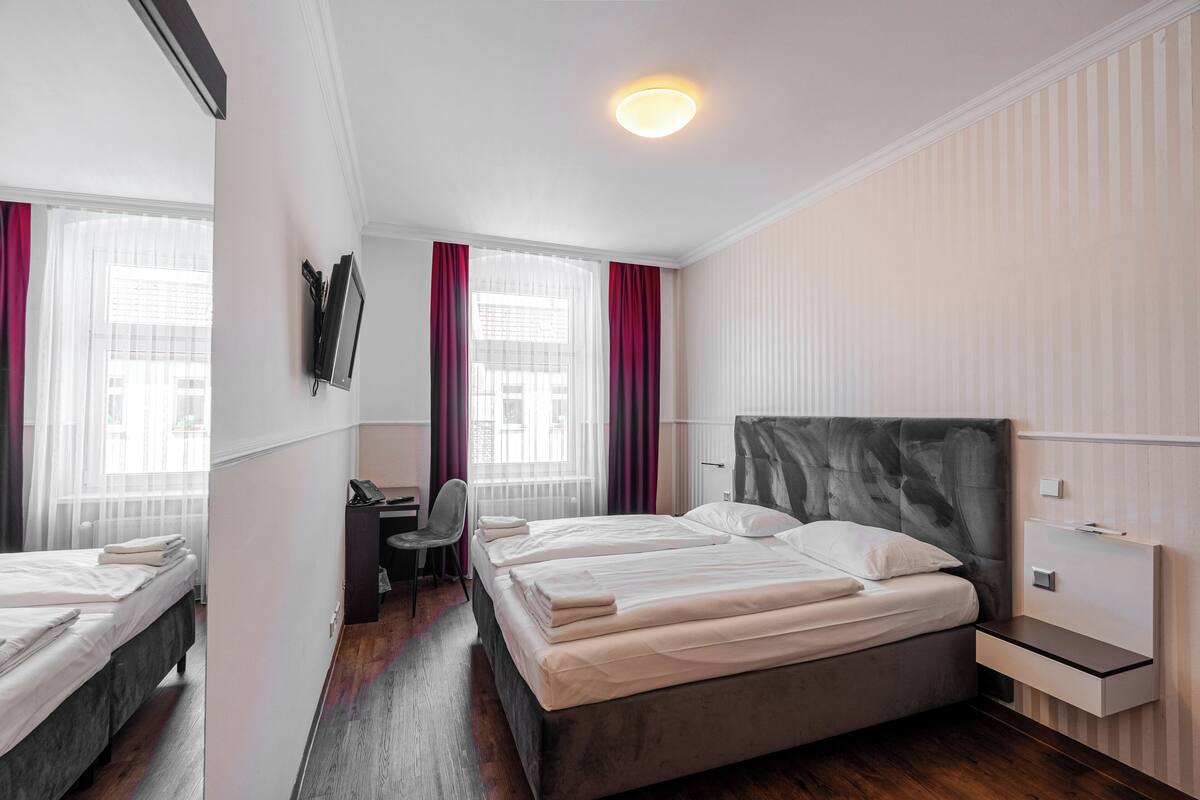 A modern hotel room with two beds, a desk, and a chair.