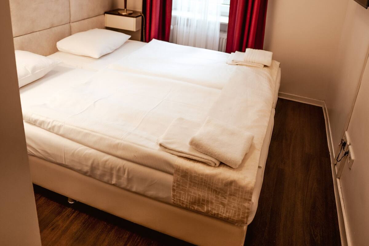 A neatly made bed with white linens and a folded towel, a bedside lamp, and a framed picture on the wall.