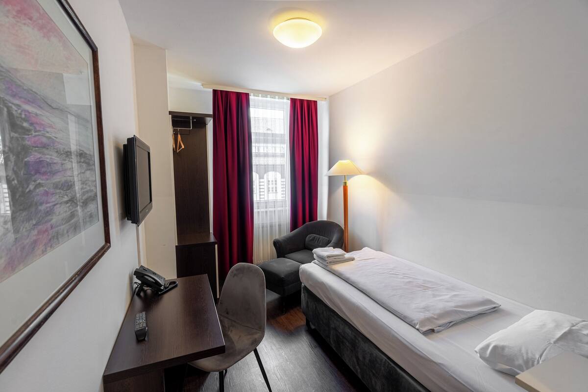 A hotel room with a bed, desk, chair, and a TV.