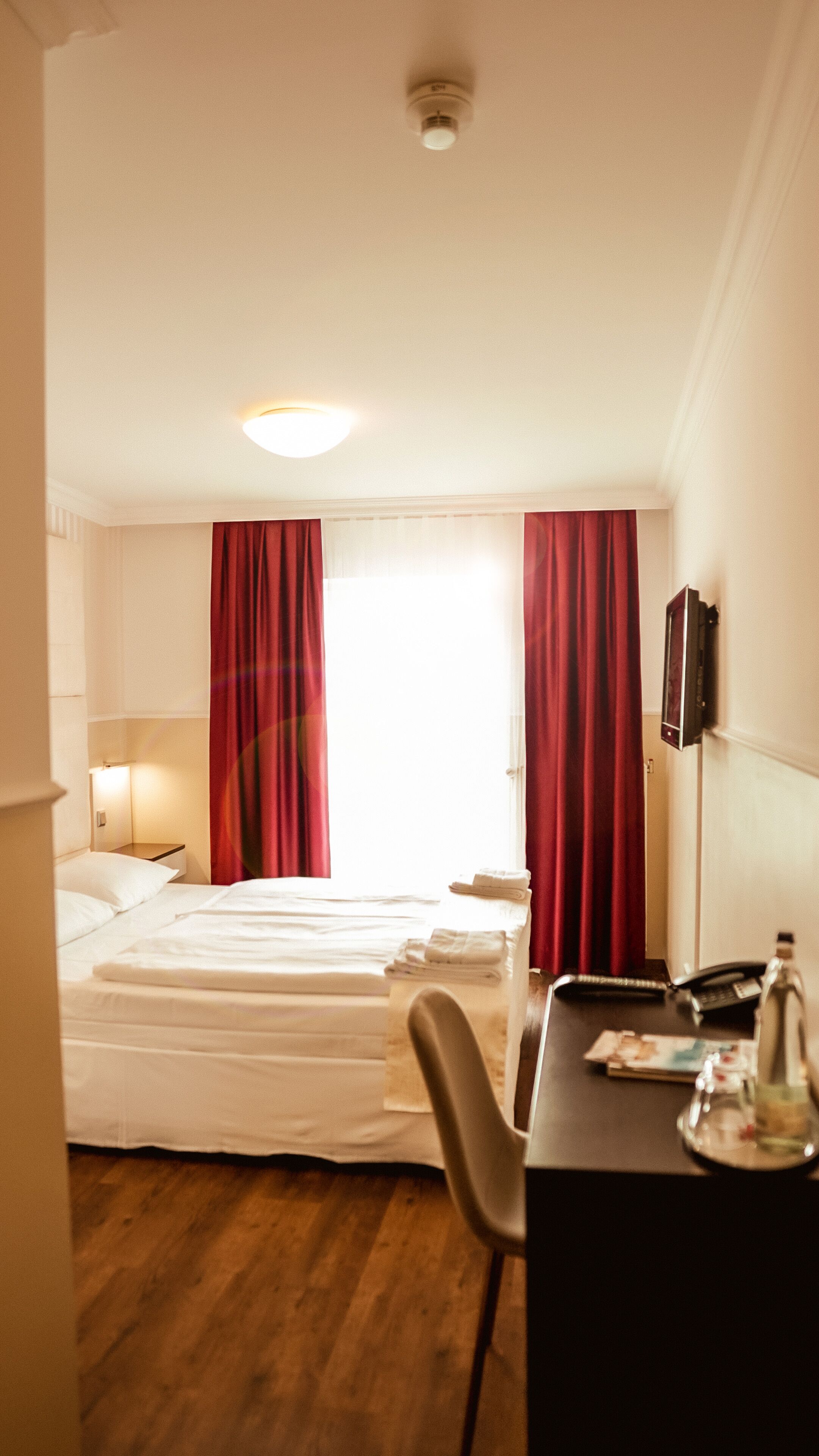 Una habitación de hotel con cama, escritorio, silla, teléfono y televisor.