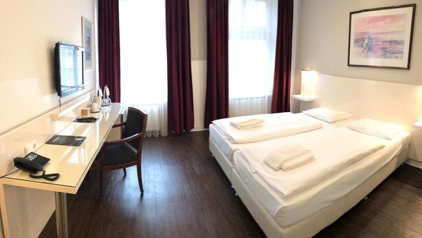 A hotel room with a bed, a desk, a chair, a phone, and a window with curtains. - Hotel Prens Berlin (Berlin)