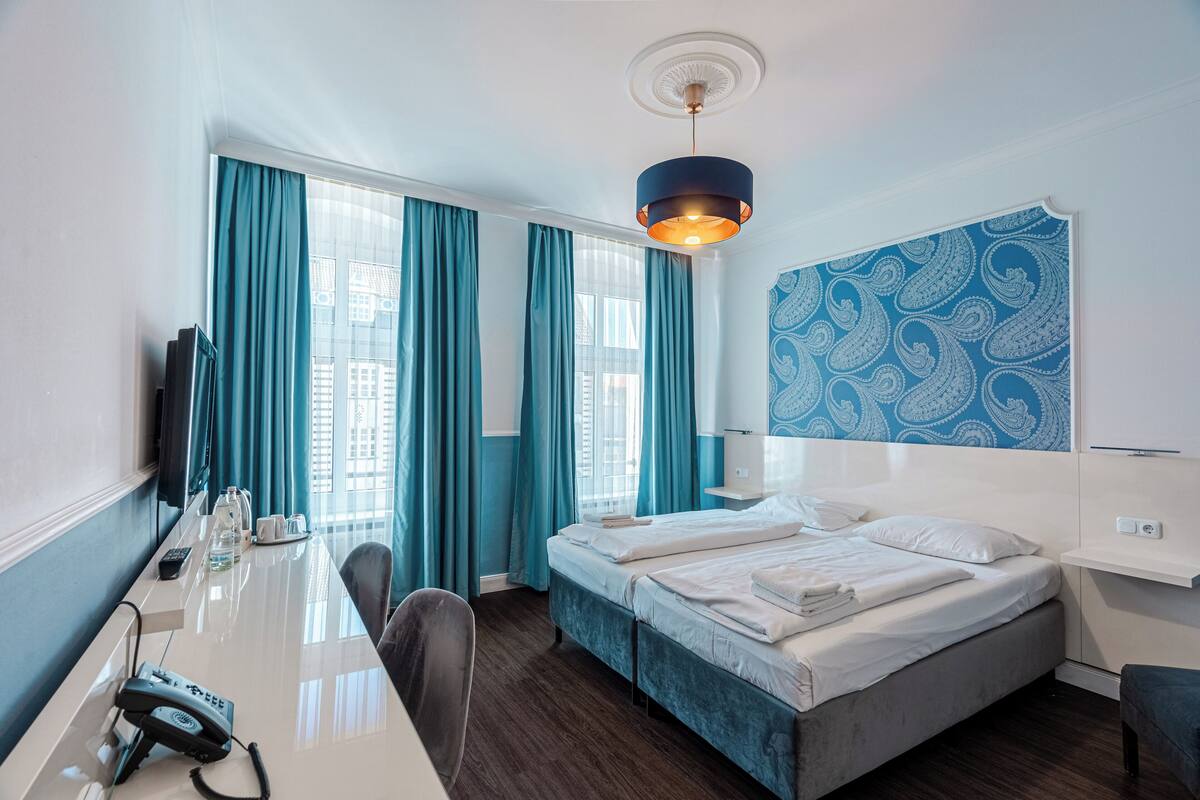 A hotel room with a desk, two beds, a TV, and a patterned wall.