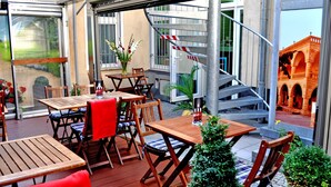 An outdoor patio with wooden tables and chairs, a small Christmas tree, and a view of a building with arches. - Hotel Prens Berlin (Berlin)