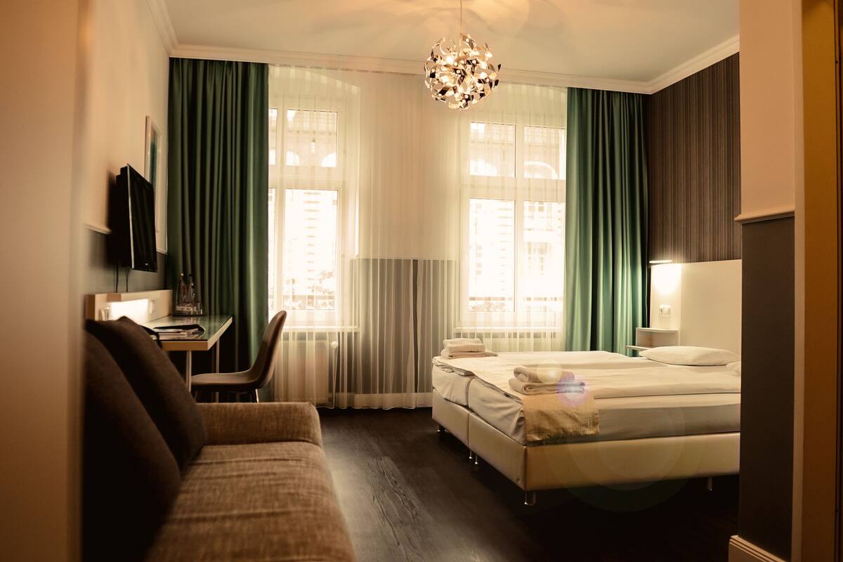 A hotel room with a bed, a desk, a chair, a TV, and a chandelier.