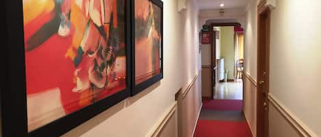 Un pasillo con alfombra roja, paredes blancas y arte abstracto enmarcado a la izquierda.