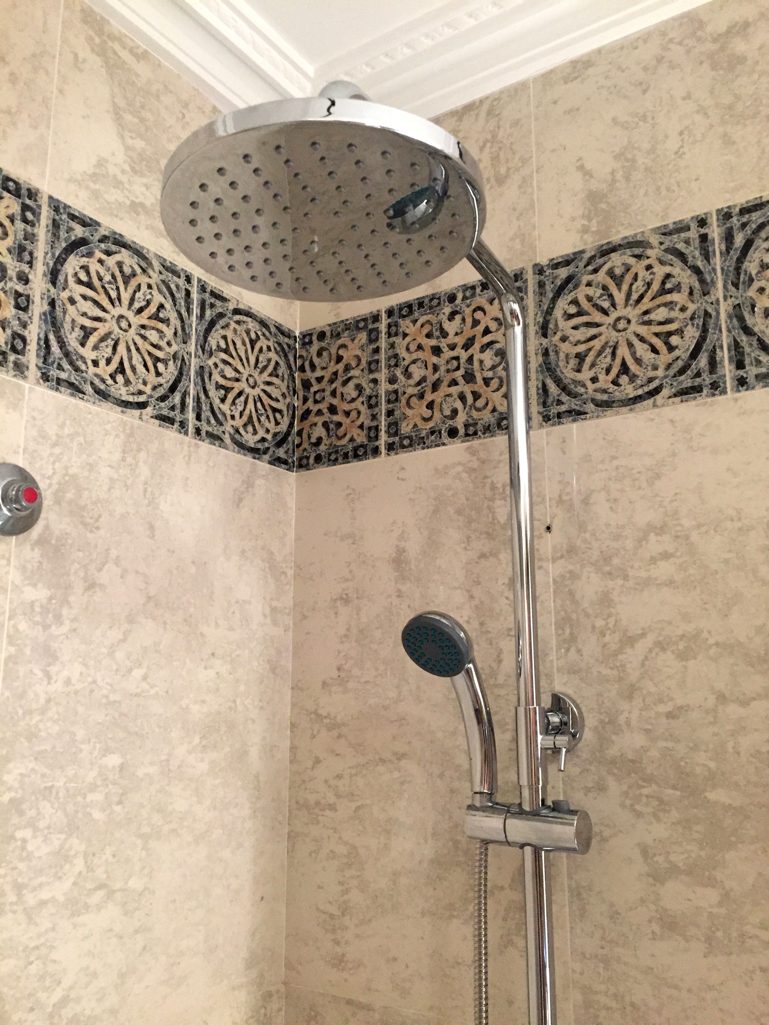 A shower with a handheld showerhead and a fixed overhead showerhead in a corner with decorative tile borders.