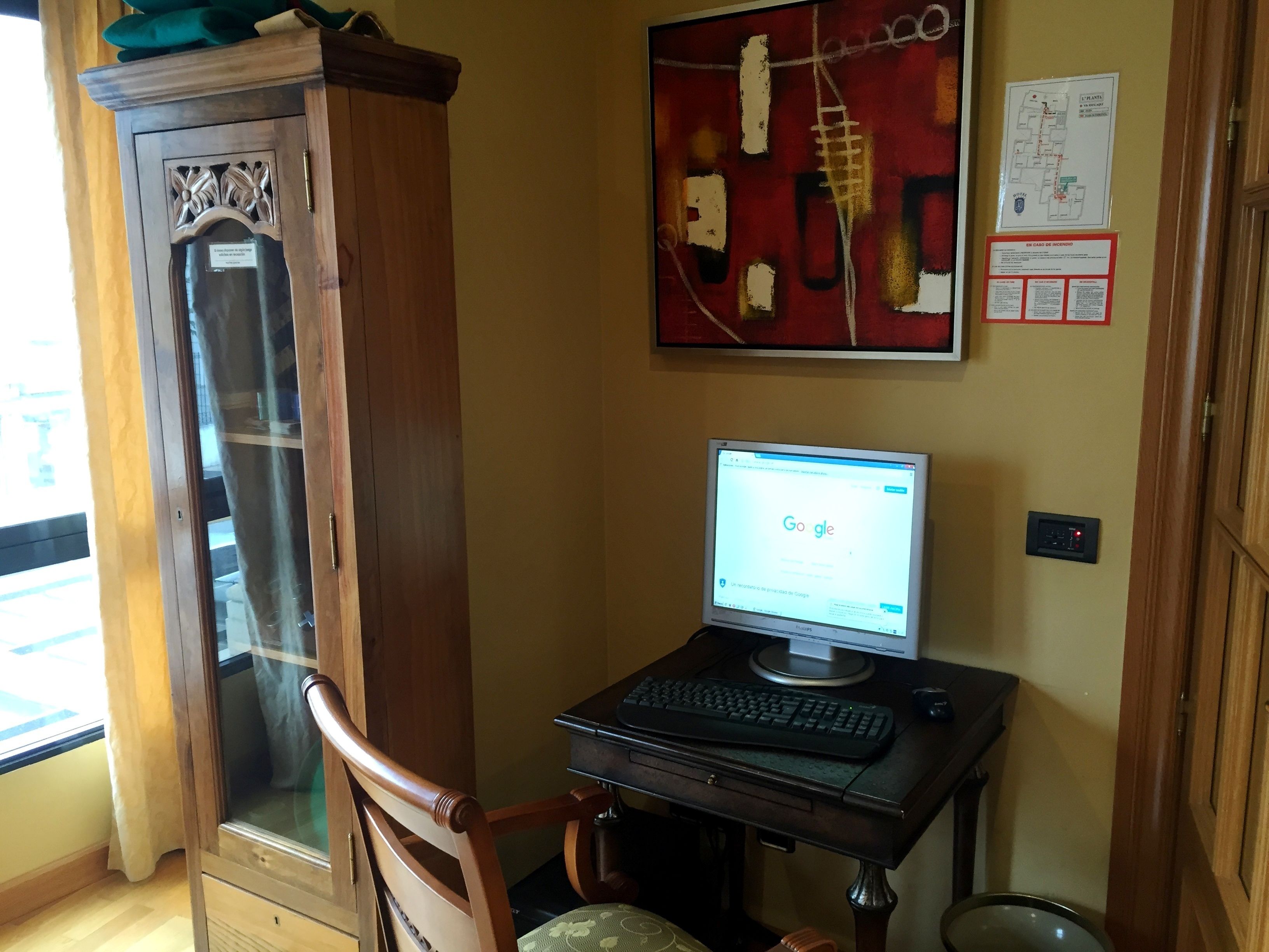Una habitación con un armario de madera, un escritorio con computadora, una silla y una ventana con cortinas.