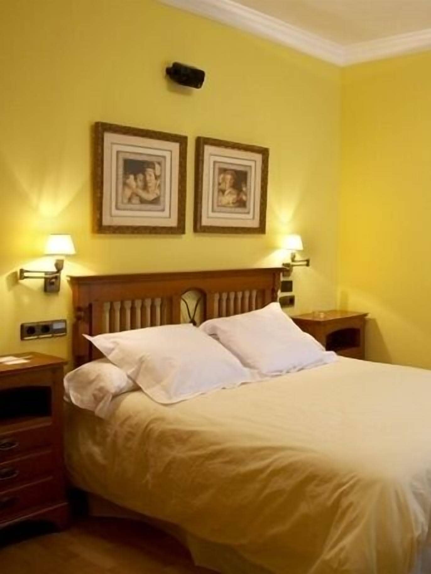 A hotel room with a large bed, two bedside tables, a wooden headboard, and two wall-mounted lamps.