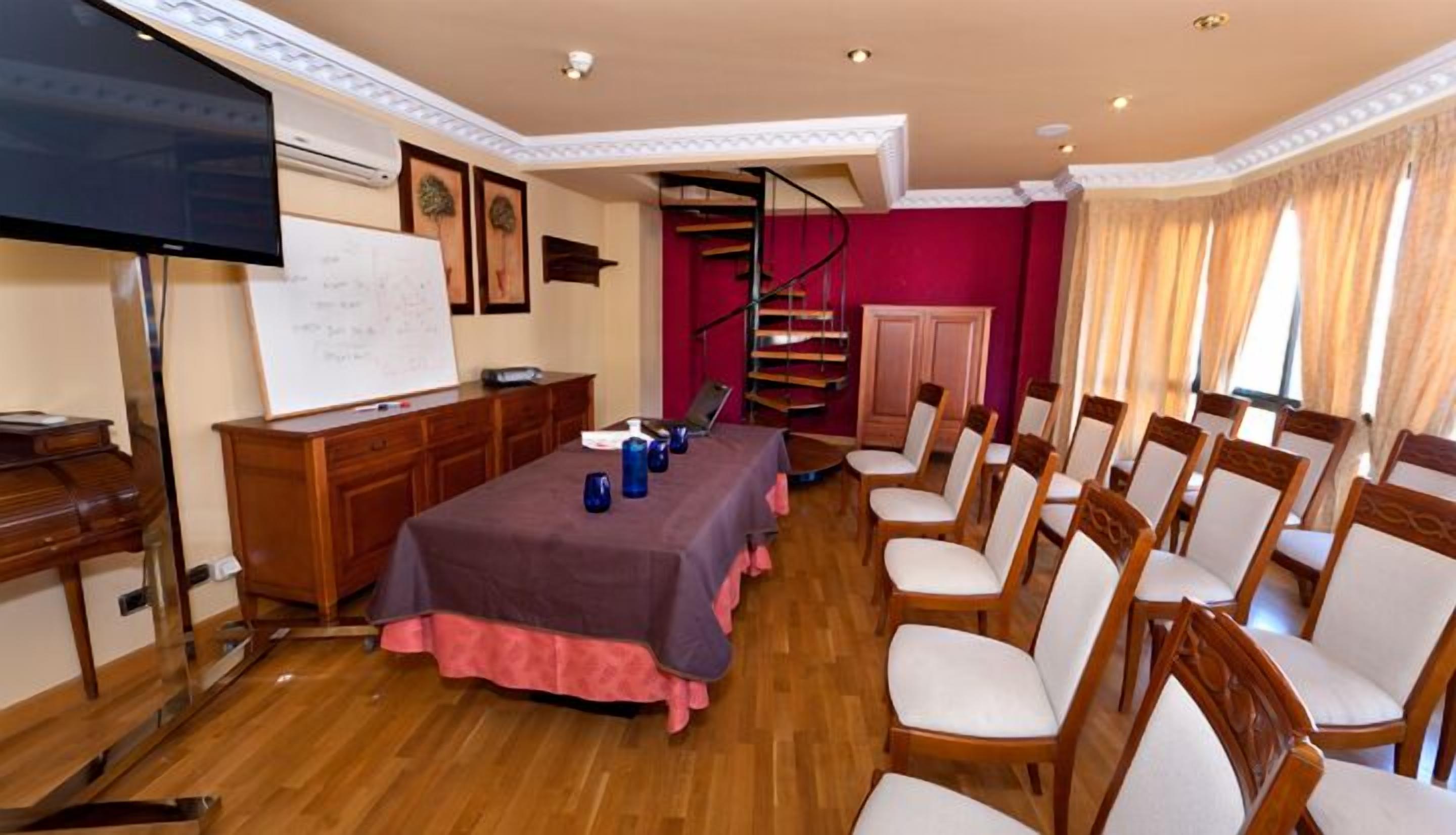 A conference room with a long table, chairs, a whiteboard, a TV, and a staircase.
