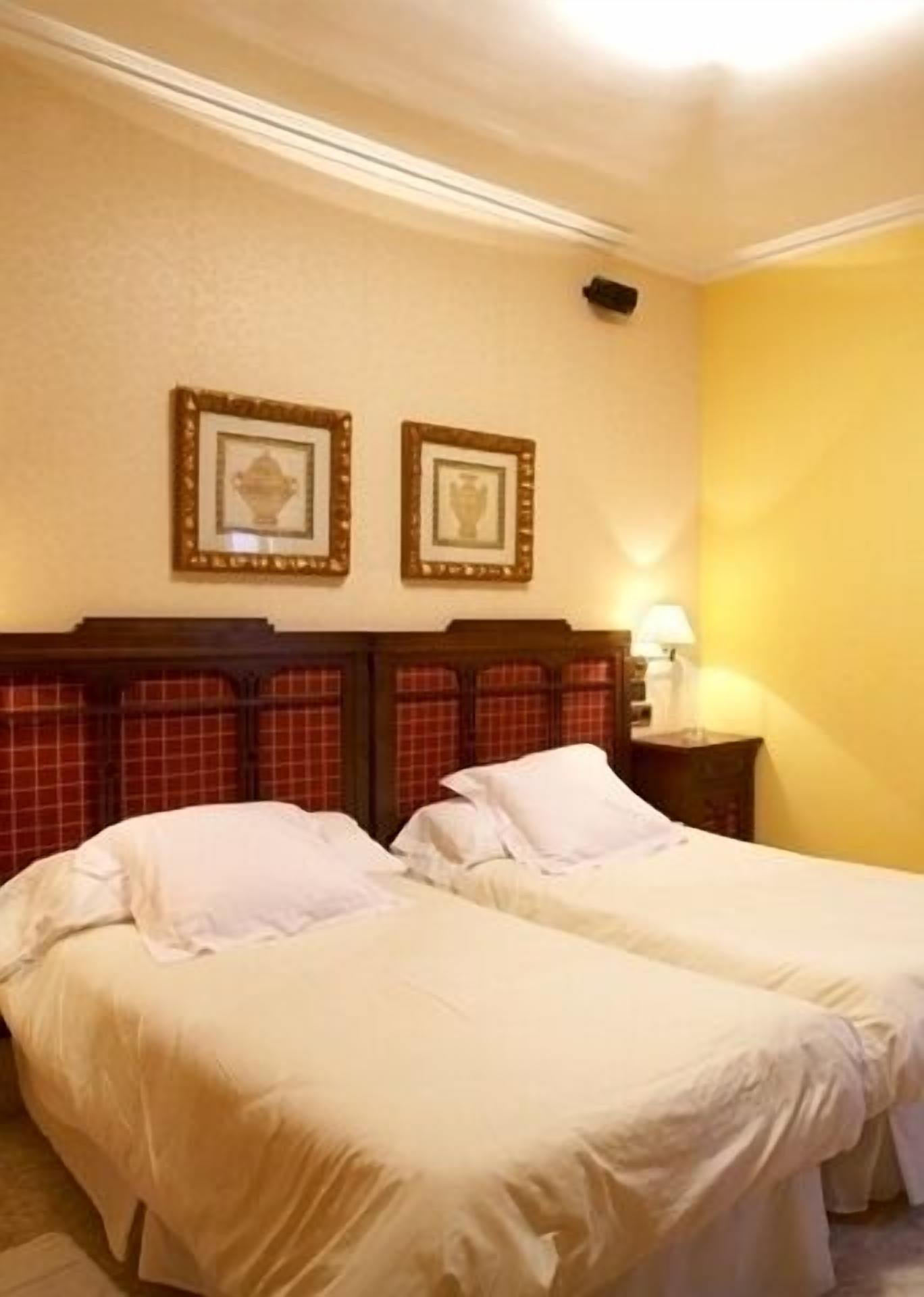 Een hotelkamer met twee bedden, een houten hoofdbord, een lamp en twee ingelijste foto's aan de muur.