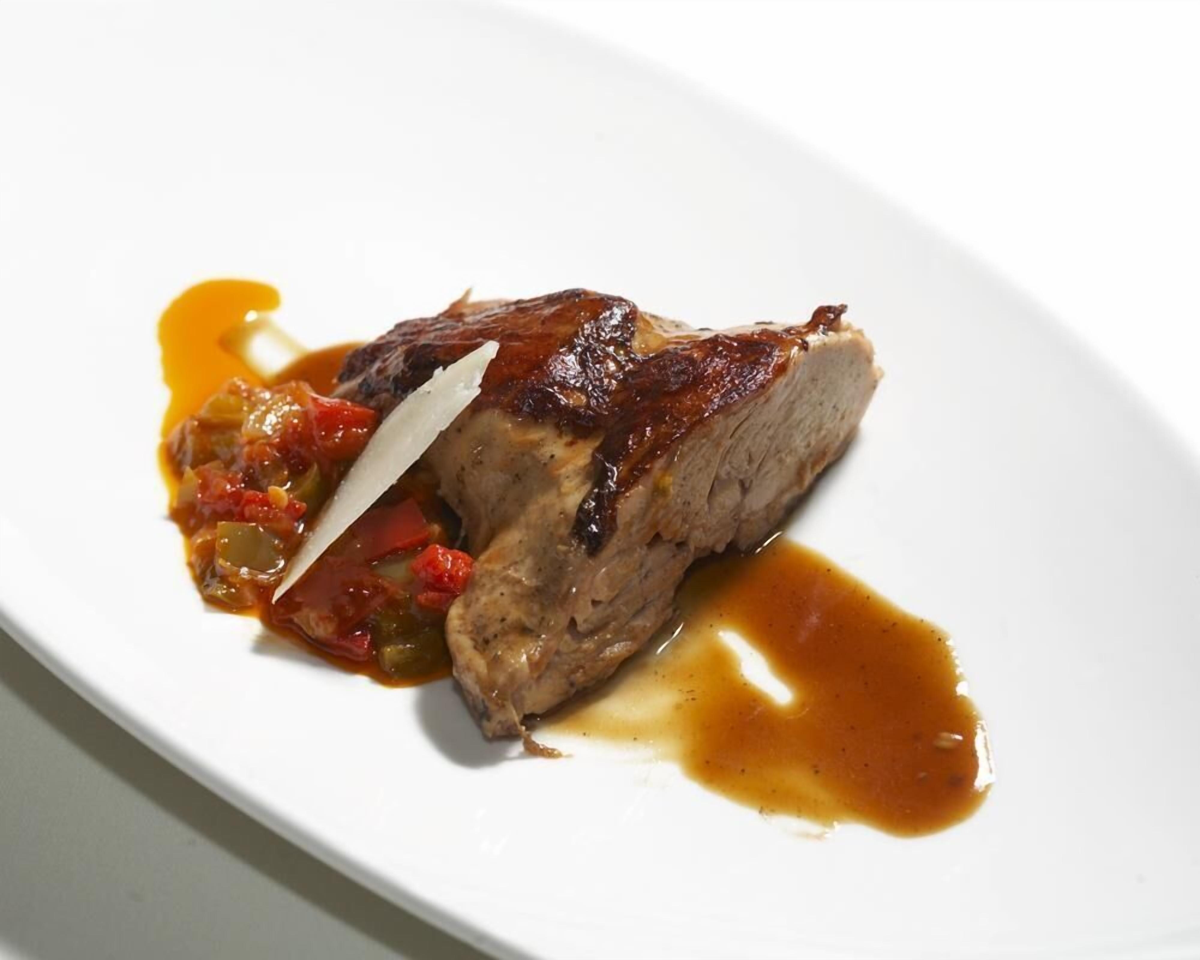 Un trozo de carne con salsa y verduras sobre un plato blanco.