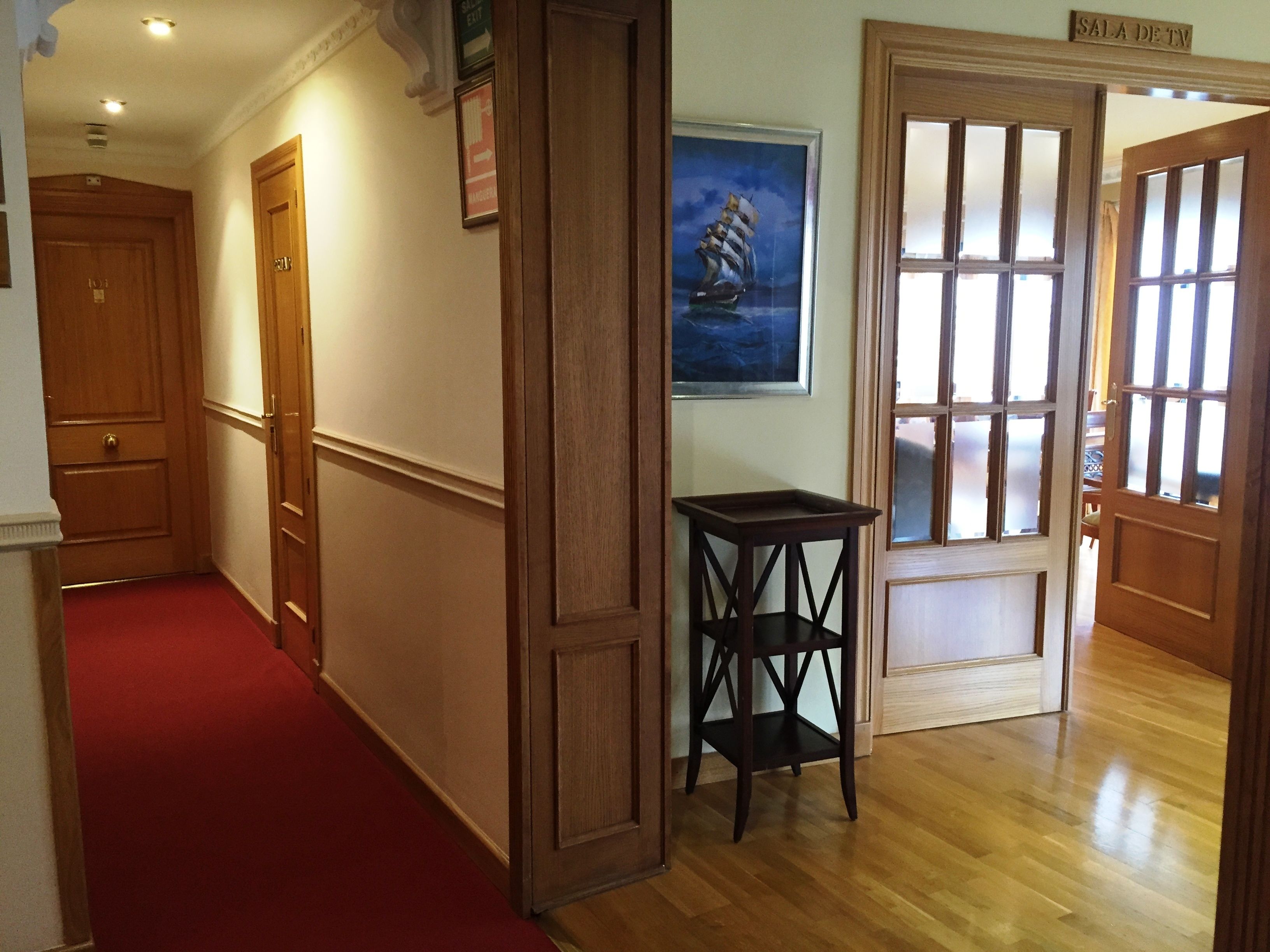 A hallway with wooden doors, a red carpet, and a framed painting of a ship.