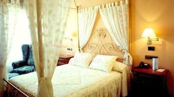 A bedroom with a four-poster bed, a canopy, a nightstand with a lamp, and a chair.
