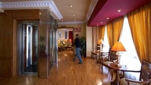 Un hall d’hôtel doté d’un plancher en bois, d’une entrée avec une porte en verre et d’un espace détente avec des tables et des chaises.