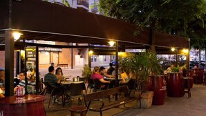 Un café en plein air avec des tables et des bancs sous une marquise, entouré de plantes en pot et offrant une vue sur la rue.