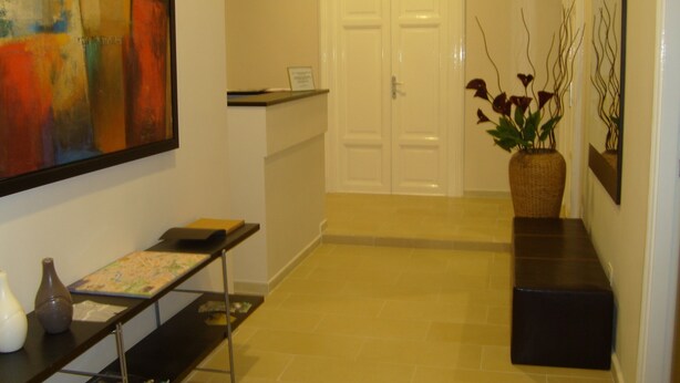A hallway with a reception desk, a door, a vase with flowers, and a painting on the wall.