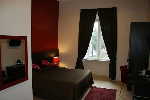 A bedroom with a bed, a red rug, a TV mounted on the wall, and a window with curtains. - Inncentral Rome (Rome)