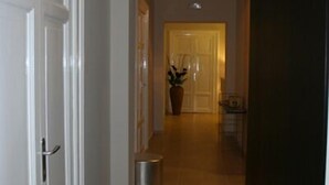 A hallway with a door on the left, a trash can, and a potted plant in the center.