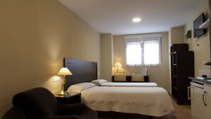 Habitación de hotel con dos camas, un escritorio, una silla, un televisor y un refrigerador.