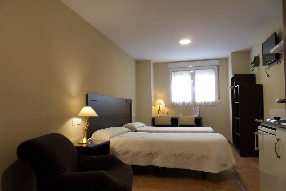 Habitación de hotel con dos camas, un escritorio, una silla, un televisor y un refrigerador.