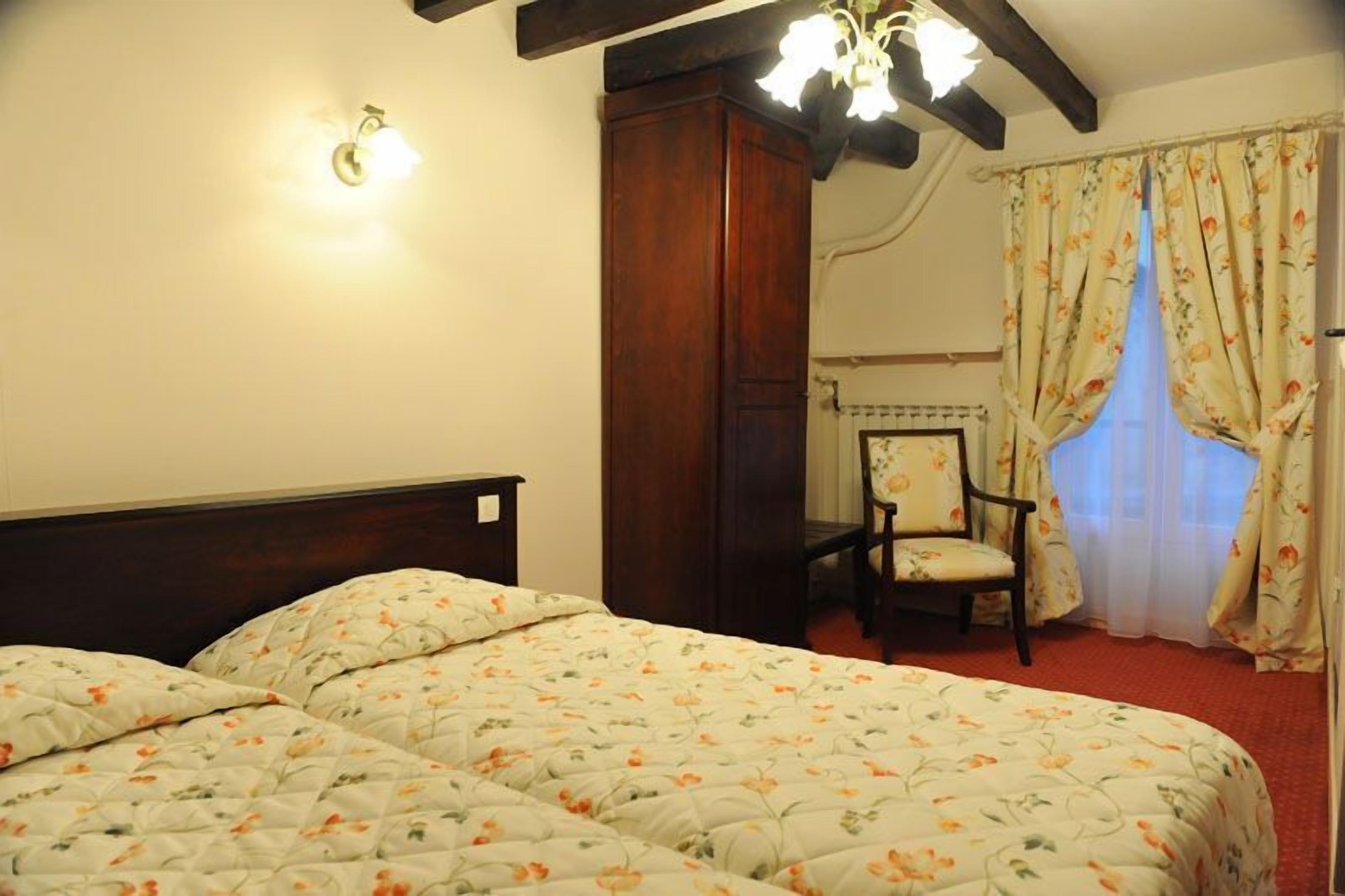 A bedroom with two beds, a wooden headboard, a chair, and a window with floral curtains.
