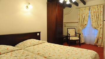 A bedroom with two beds, a wooden headboard, a chair, and a window with floral curtains.