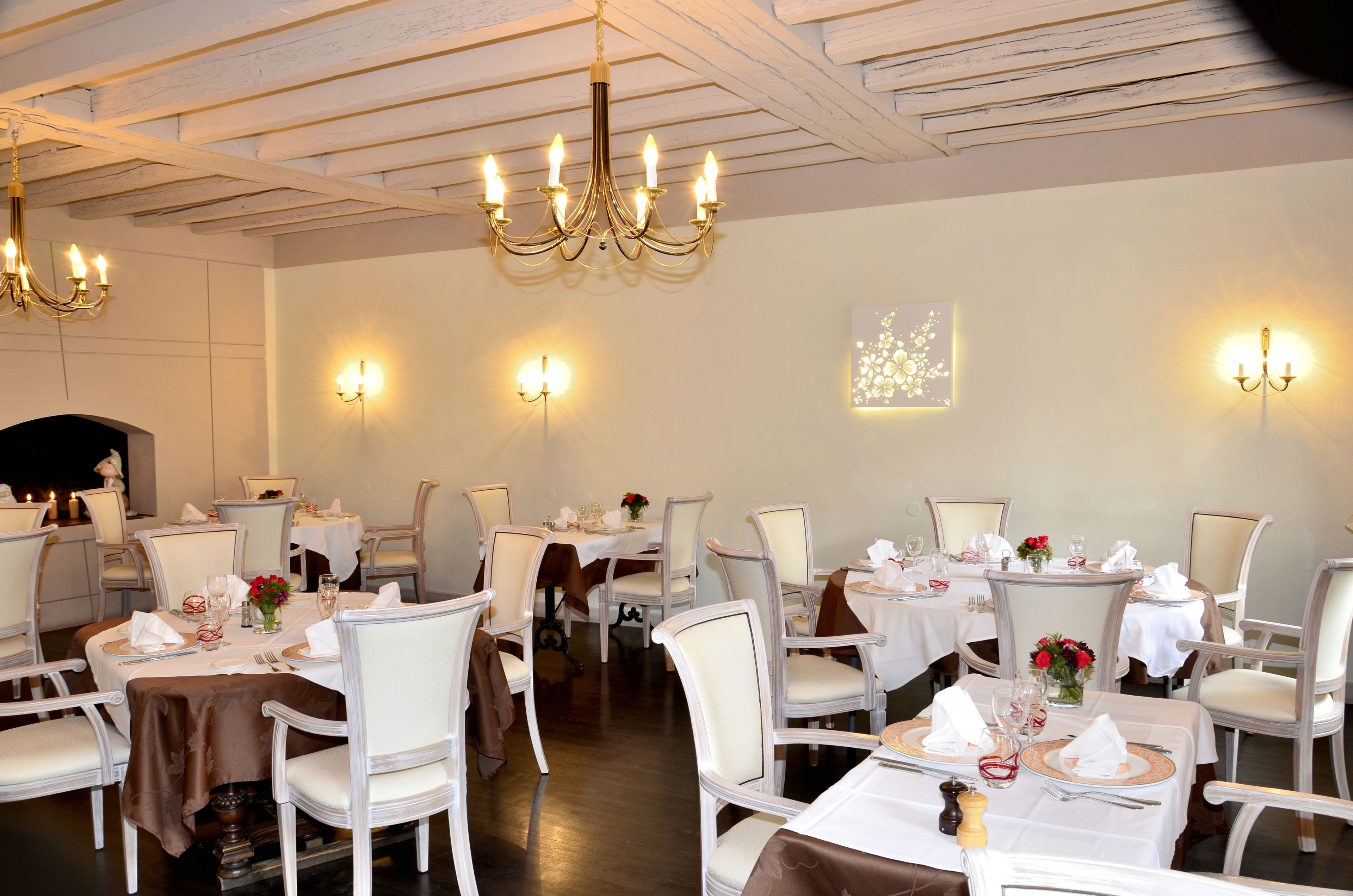 Zona pranzo con tavoli rotondi, sedie bianche, lampadari, applique e centrotavola floreali.