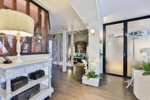 A modern interior with a white console table, leather storage, a white lamp, and a view of a living area through a glass door. - Du Sauvage (La Ferte-Gaucher)