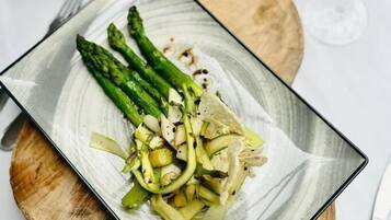Ein Teller Essen mit Spargel und einem grünen Gemüse, möglicherweise Zucchini, auf einem rechteckigen Teller mit einem Holzuntersetzer darunter.