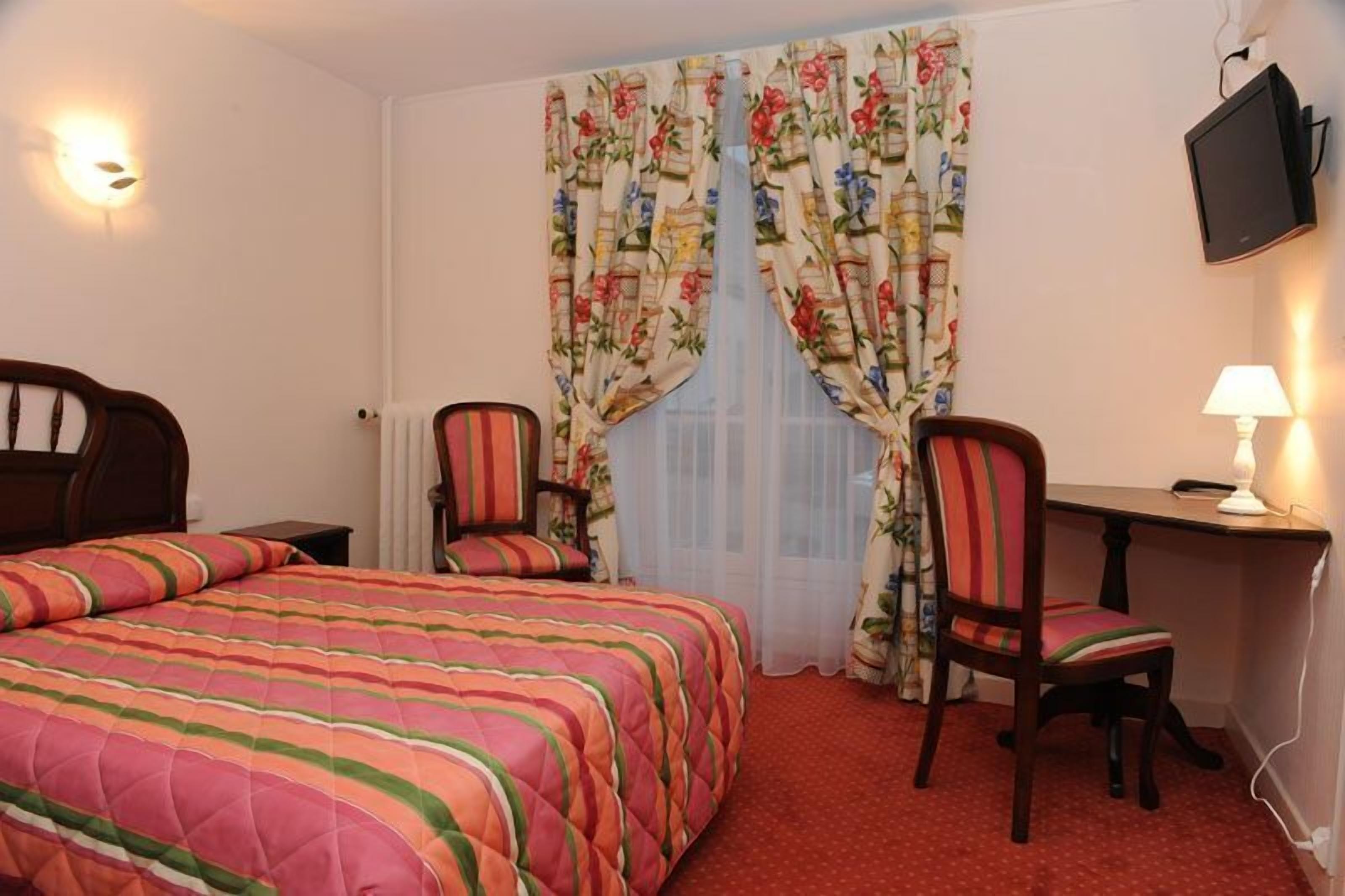 A hotel room with a bed, a desk, a chair, a TV, and curtains.