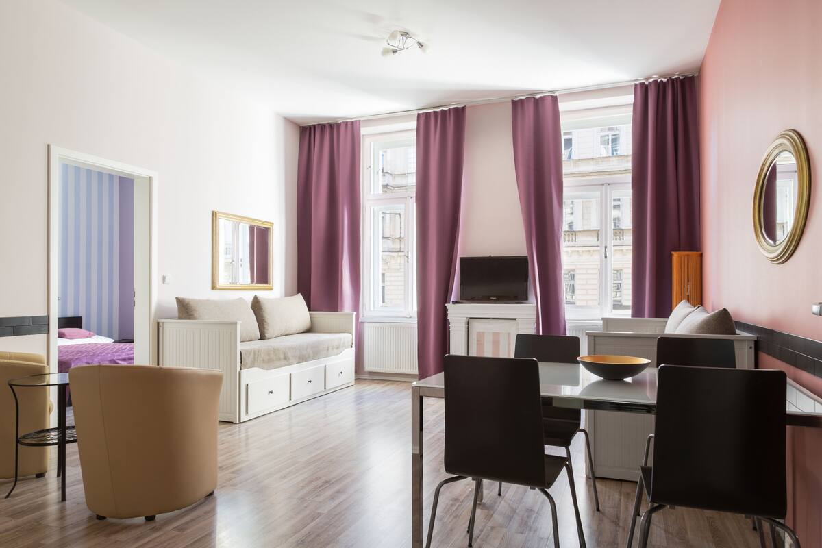 A modern living room with a sofa, dining table, and chairs. There is a TV and a fireplace.