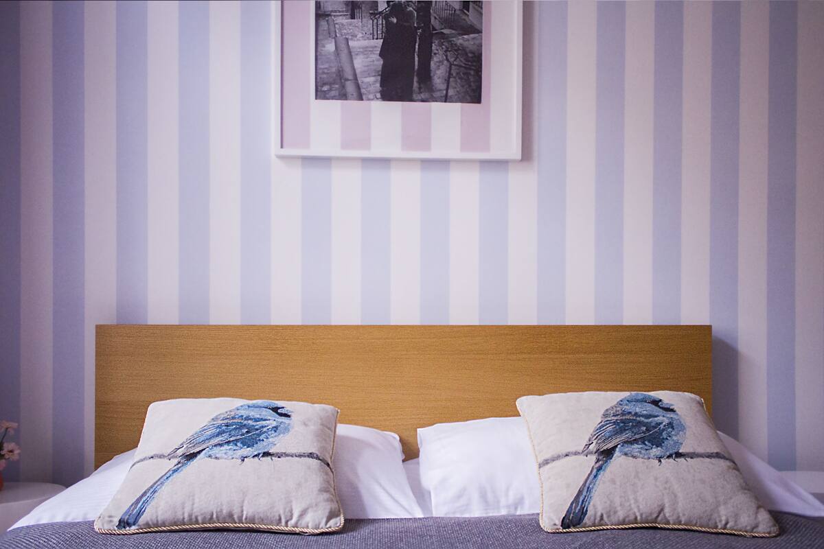 A neatly made bed with two pillows, a wooden headboard, and a striped wall with a framed picture above.