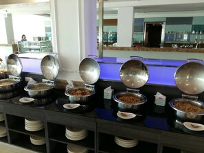 Una mesa de buffet con diferentes alimentos en recipientes metálicos, cada uno con tapa.
