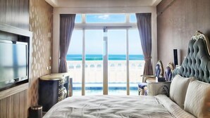 Habitación de hotel moderna con una cama grande, un televisor en la pared y vistas a la playa a través de las ventanas.