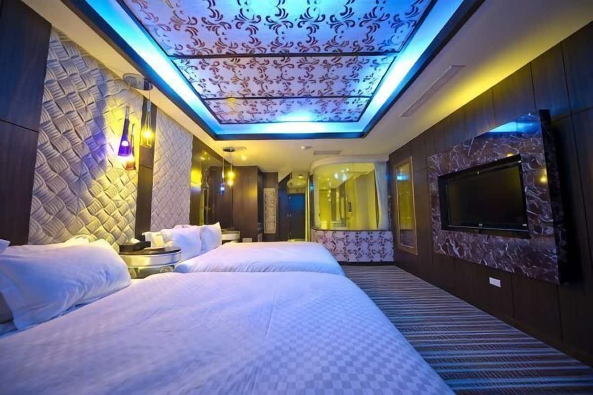 A hotel room with two beds, a flat-screen TV, a ceiling with a patterned design, and a large mirror.
