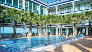 Una piscina con palmeras y un edificio con balcones al fondo.