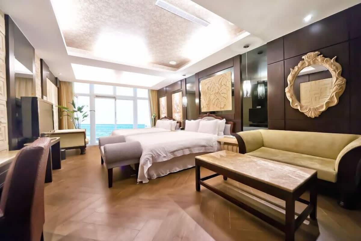 A modern hotel room with a large bed, a sofa, a desk, and a view of the ocean.