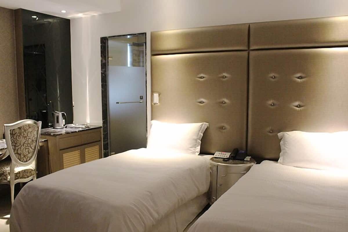 A hotel room with two beds, a desk, a chair, and a minibar.