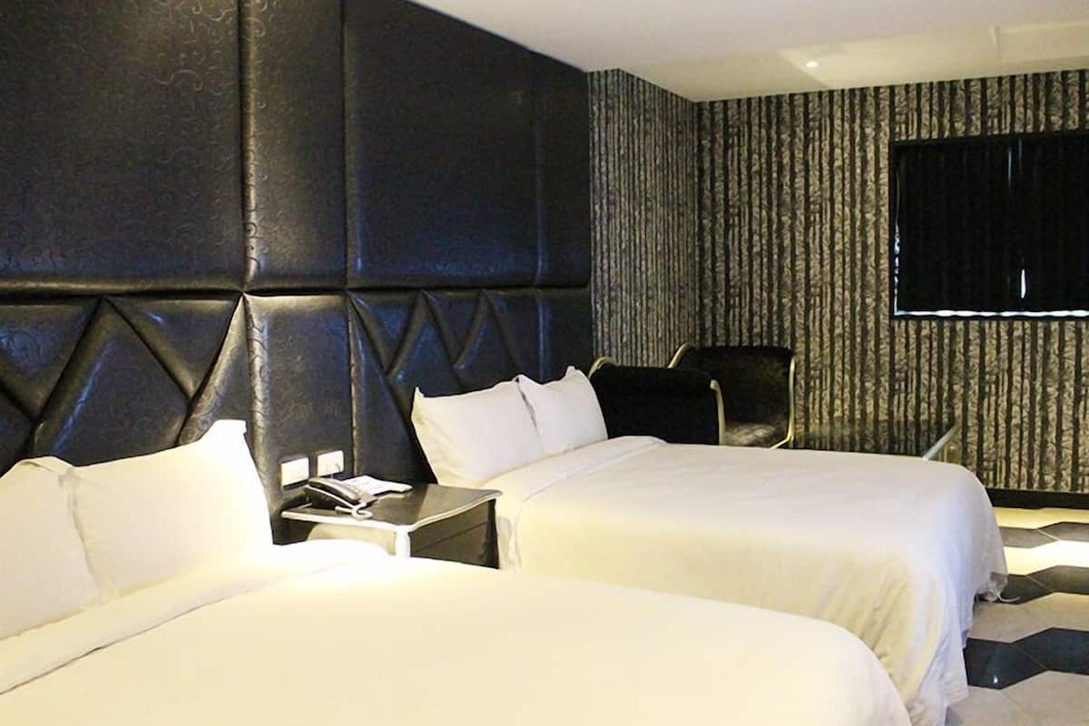A hotel room with two beds, a large padded headboard, a flat-screen TV, and a patterned wall.