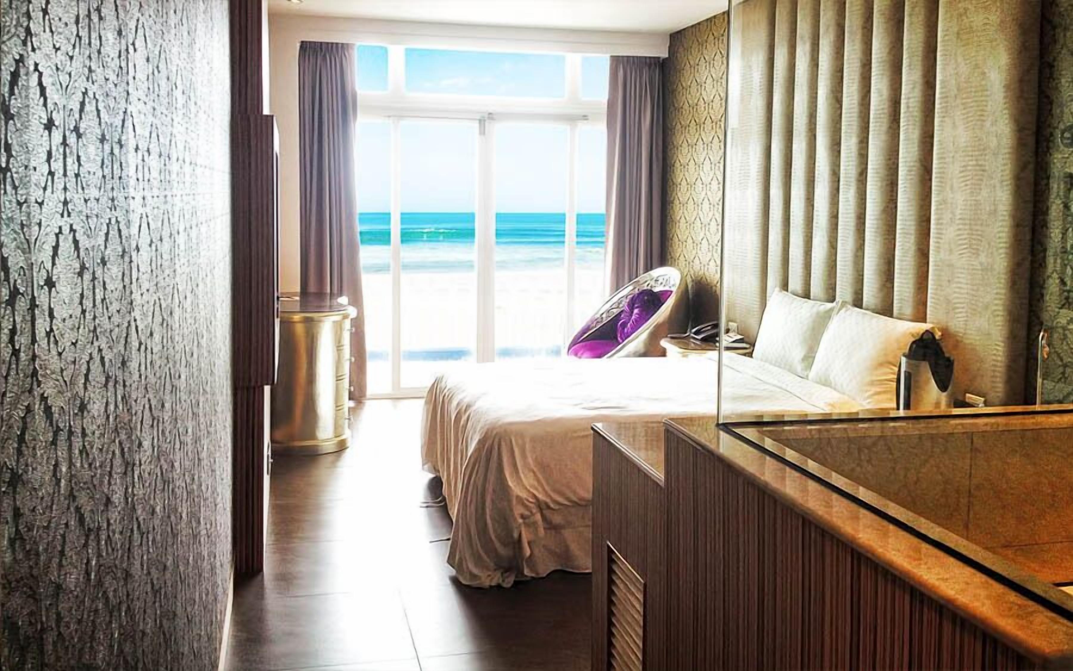 A hotel room with a bed, a vanity, and a view of the ocean.
