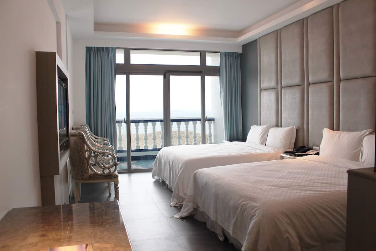 A hotel room with two beds, a desk, and a view of the beach.