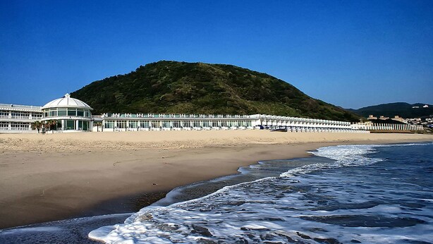 Una playa con un edificio en forma de cúpula y una hilera de construcciones frente al mar.