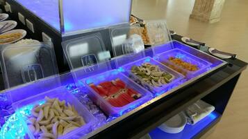 Buffet com diversos alimentos em recipientes transparentes, gelo e iluminação azul.