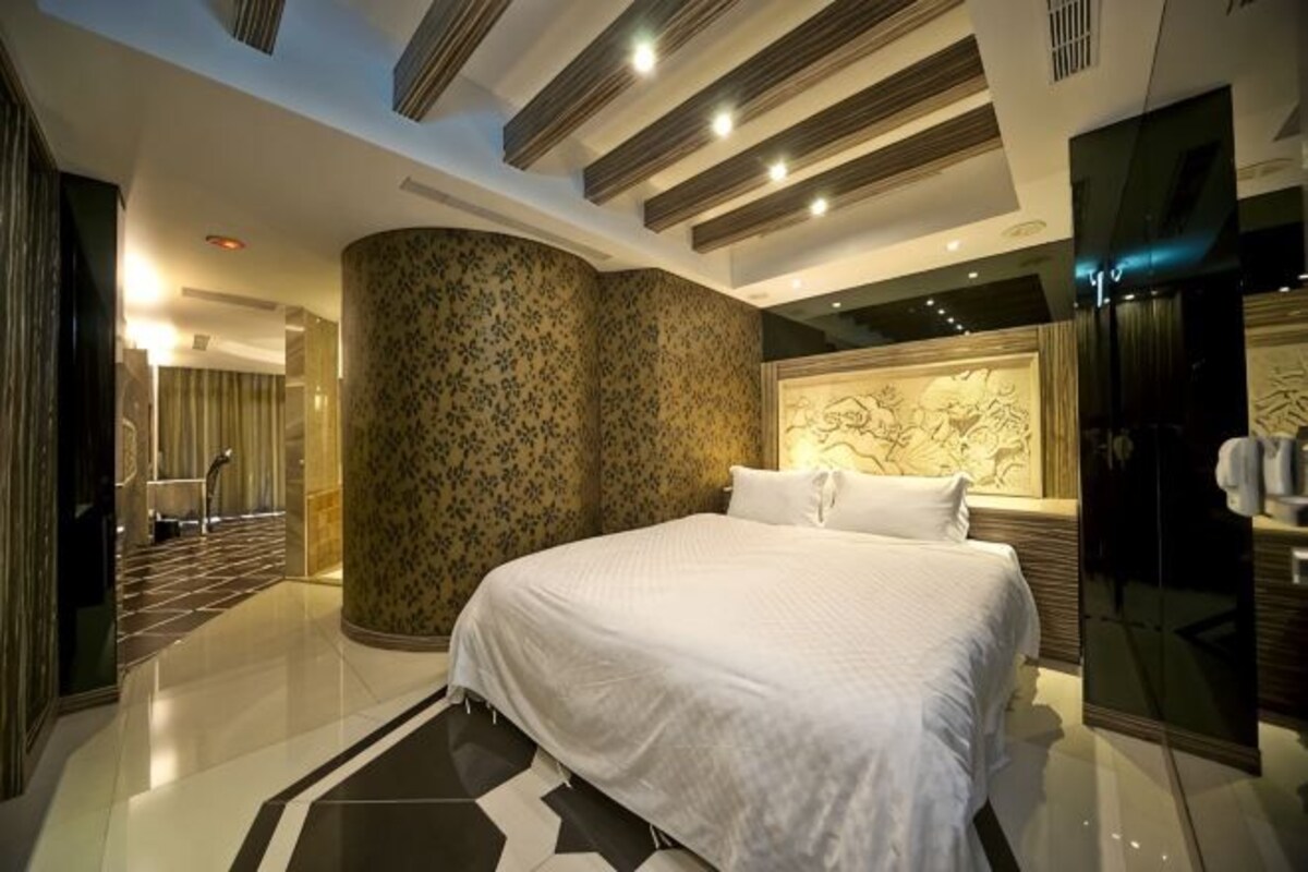 A modern bedroom with a large bed, a curved wall with a floral pattern, and a mirrored wardrobe.