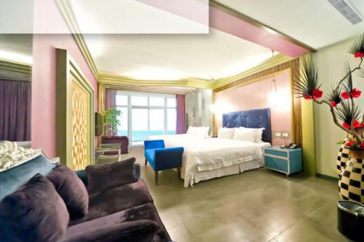 A hotel room with a bed, a blue armchair, a small table, and a potted plant.